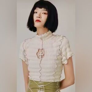 Off white, high neck, short sleeve top with a cut-out with a Cross